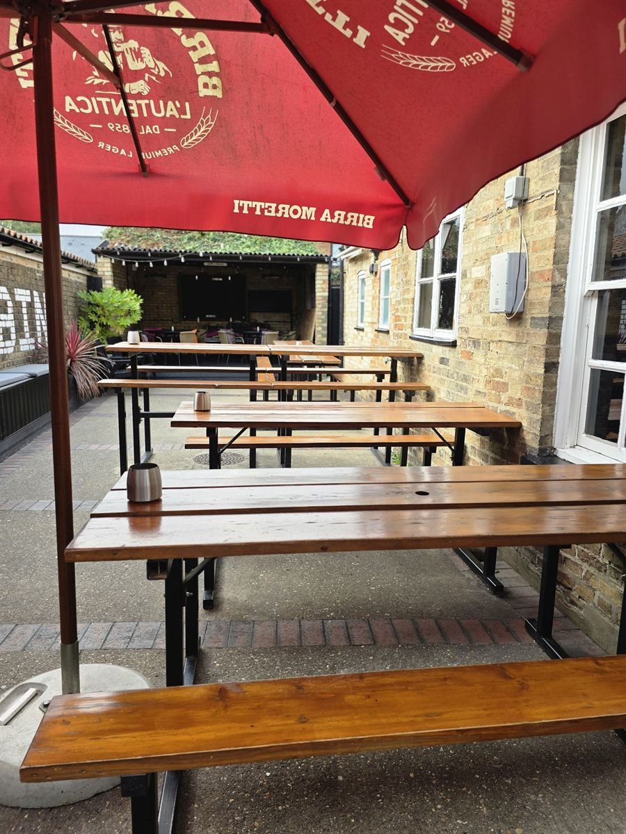 Wooden bench tables under a red parasol in the courtyard