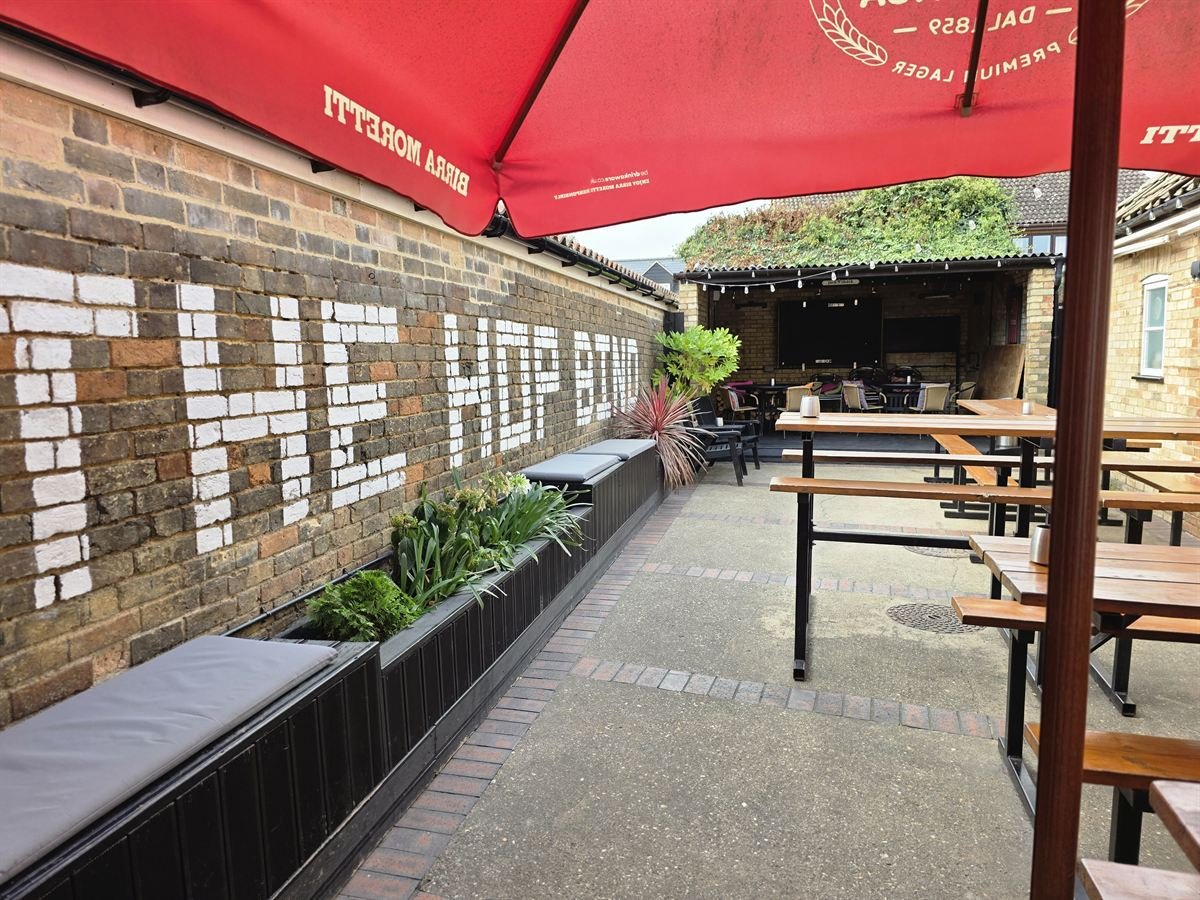 The courtyard from under a parasol, with bench tables leading to the covered seating area