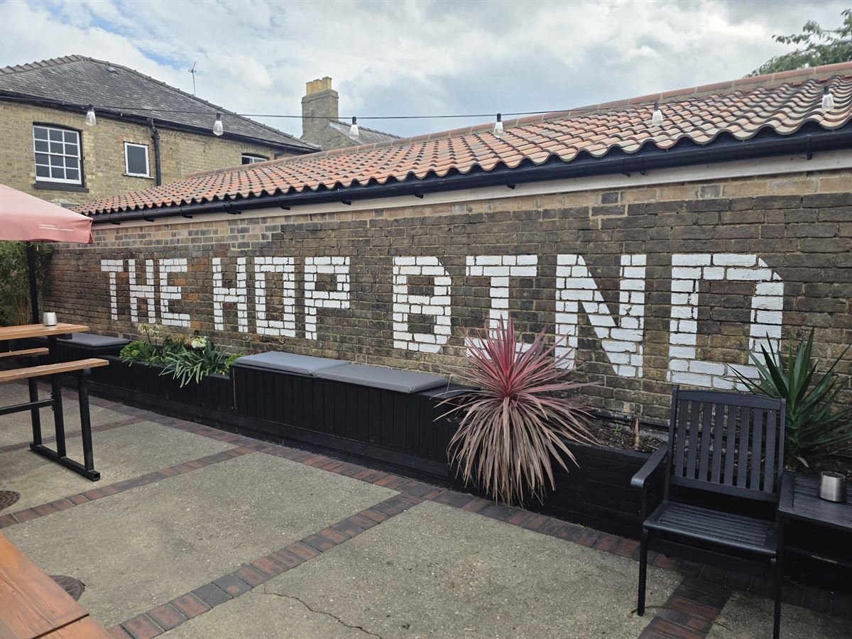 The courtyard, with THE HOP BIND painted in white along the brick wall above cushioned benches and planters