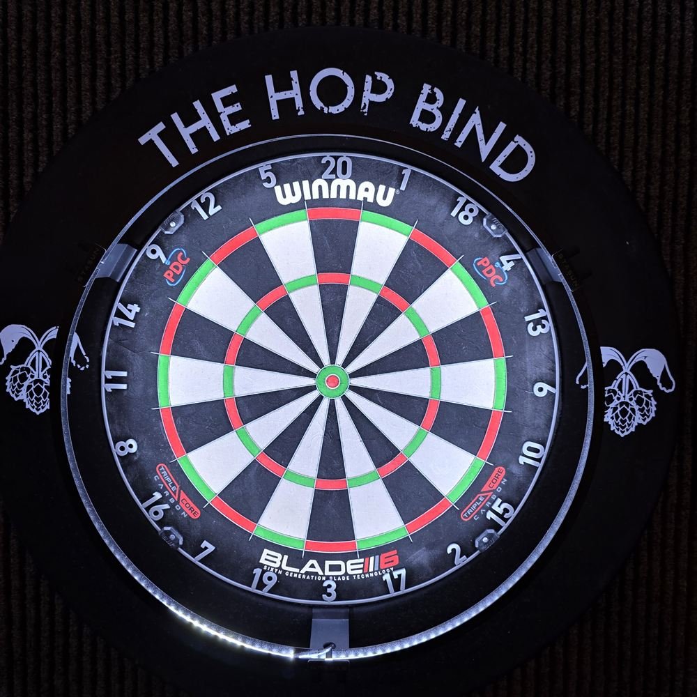 The Hop Bind's dartboard in its lit surround, printed with the pub's name and hop logo